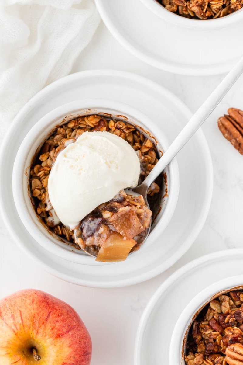 air fryer apple crisp in a ramekin with a scoop of vanilla ice cream and a spoon