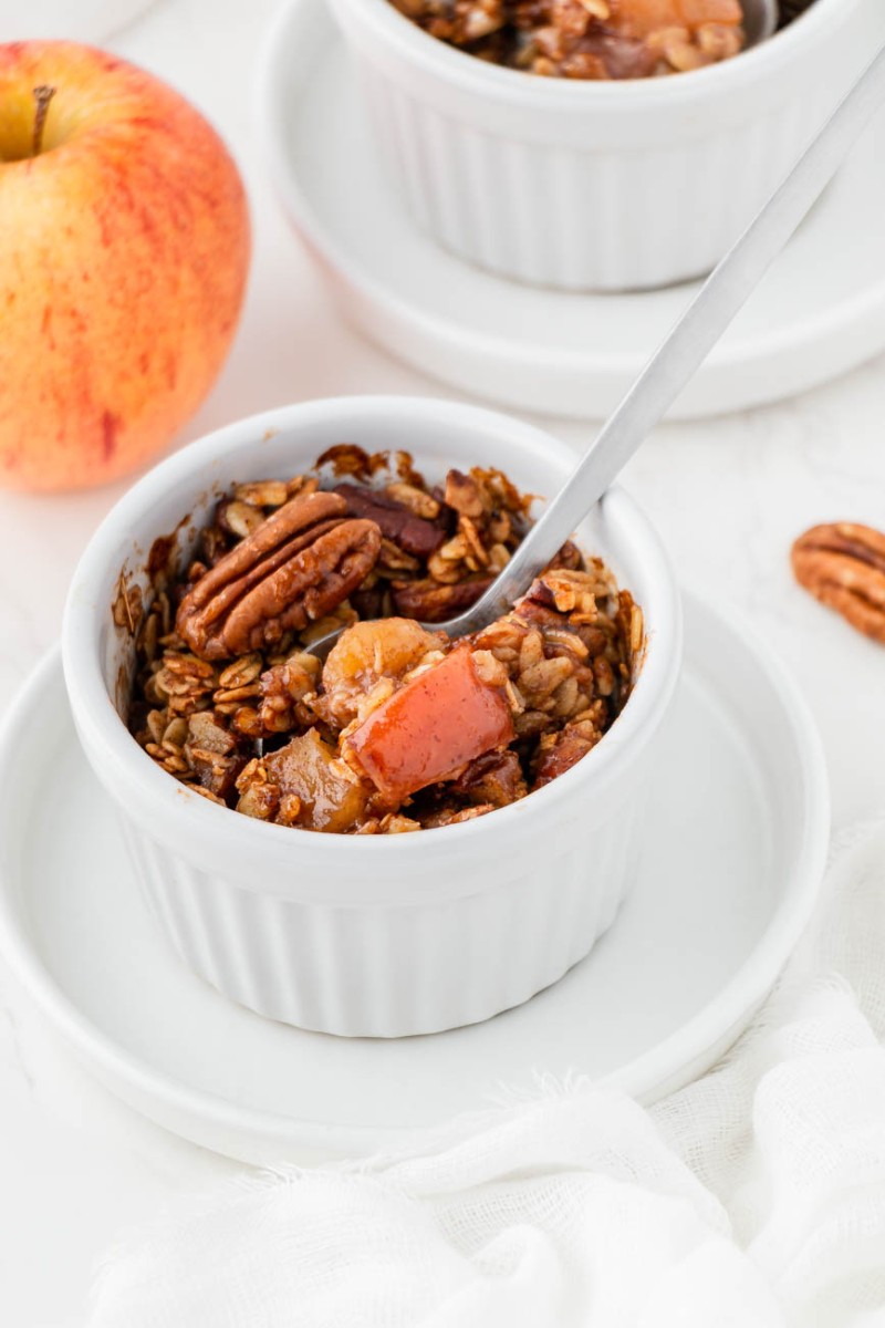 close up of mini apple crisp in a white ramekin with a spoon taking a bite out of it