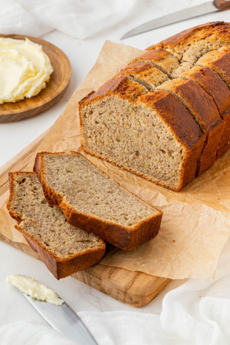 a sliced loaf of banana bread with butter and a knife on the side