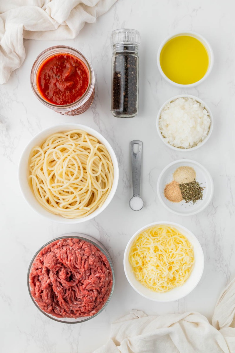 spaghetti, ground beef, tomato sauce, cheese, herbs, and olive oil in small ingredient bowls
