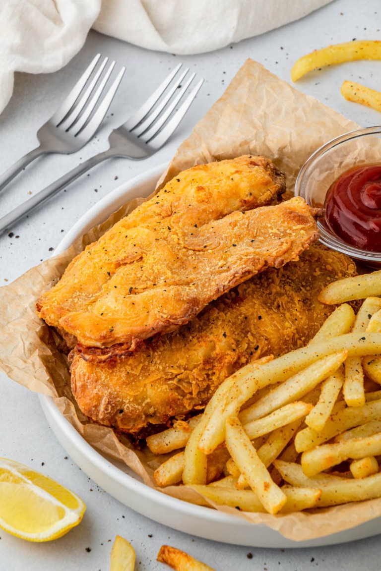 air fryer beer battered fish on a plate with french fries and ketchup with two forks to the side.