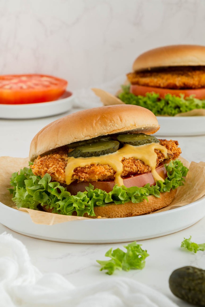 two air fryer chicken sandwiches on white plates with tomatoes in the background