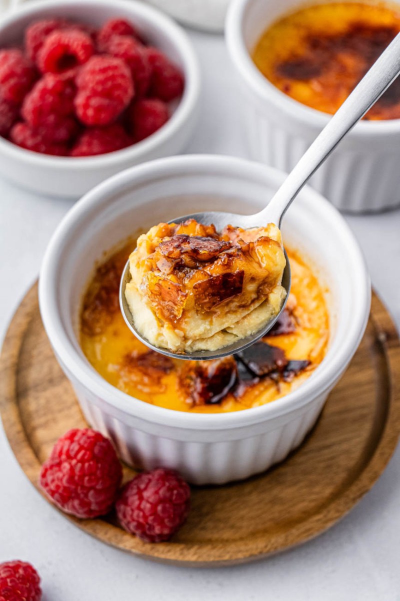 a bite of creme brulee on a poon with raspberries in the background