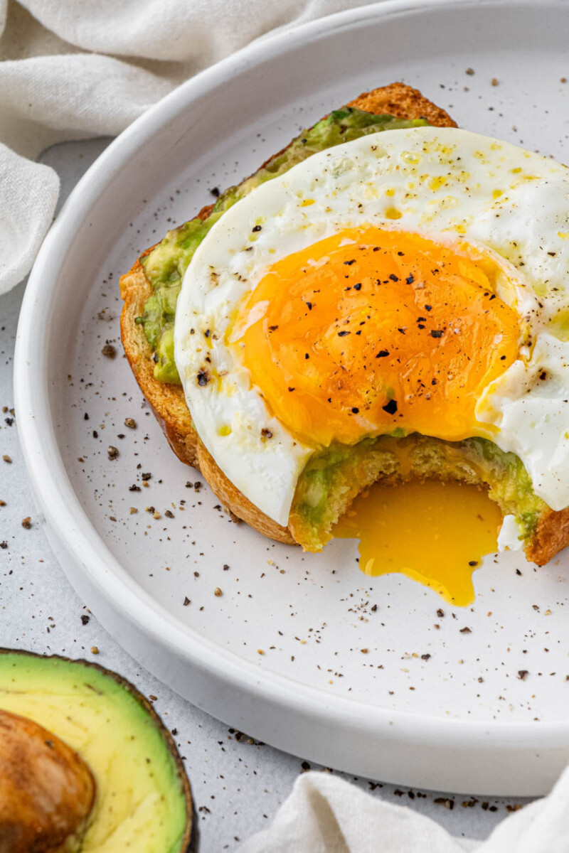 fried egg avocado toast on a plate with a bite taken