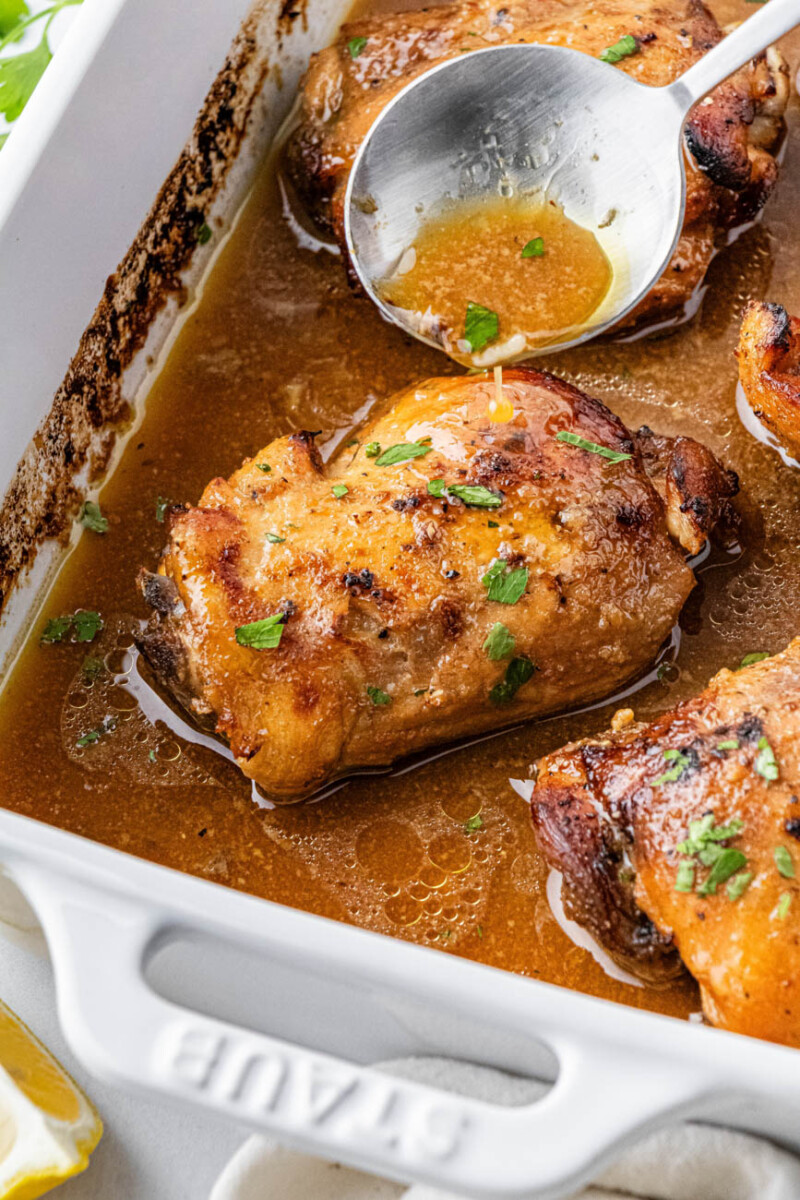 spooning marinade over chicken thighs in a baking dish