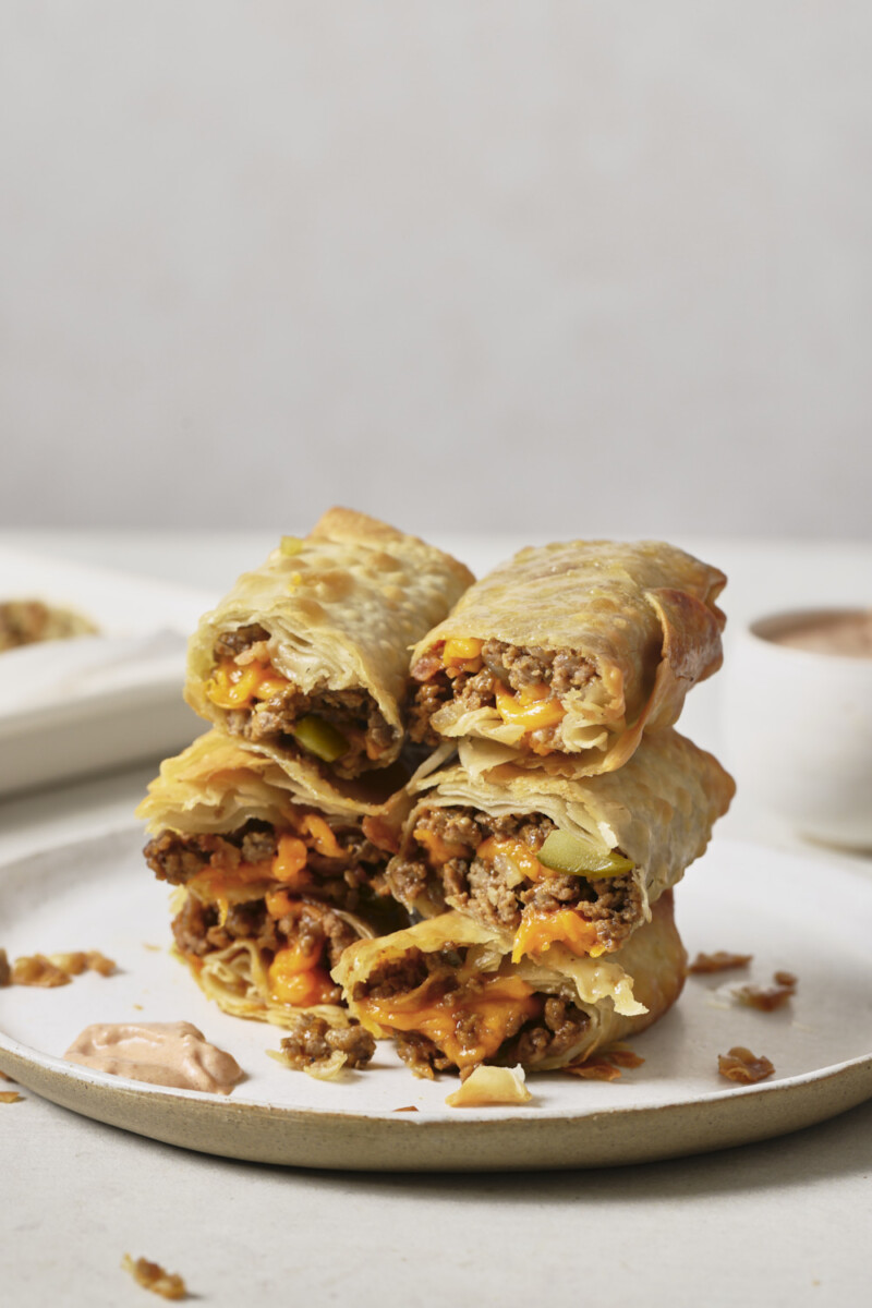 air fryer cheeseburger egg rolls sliced in half and stacked on a white plate