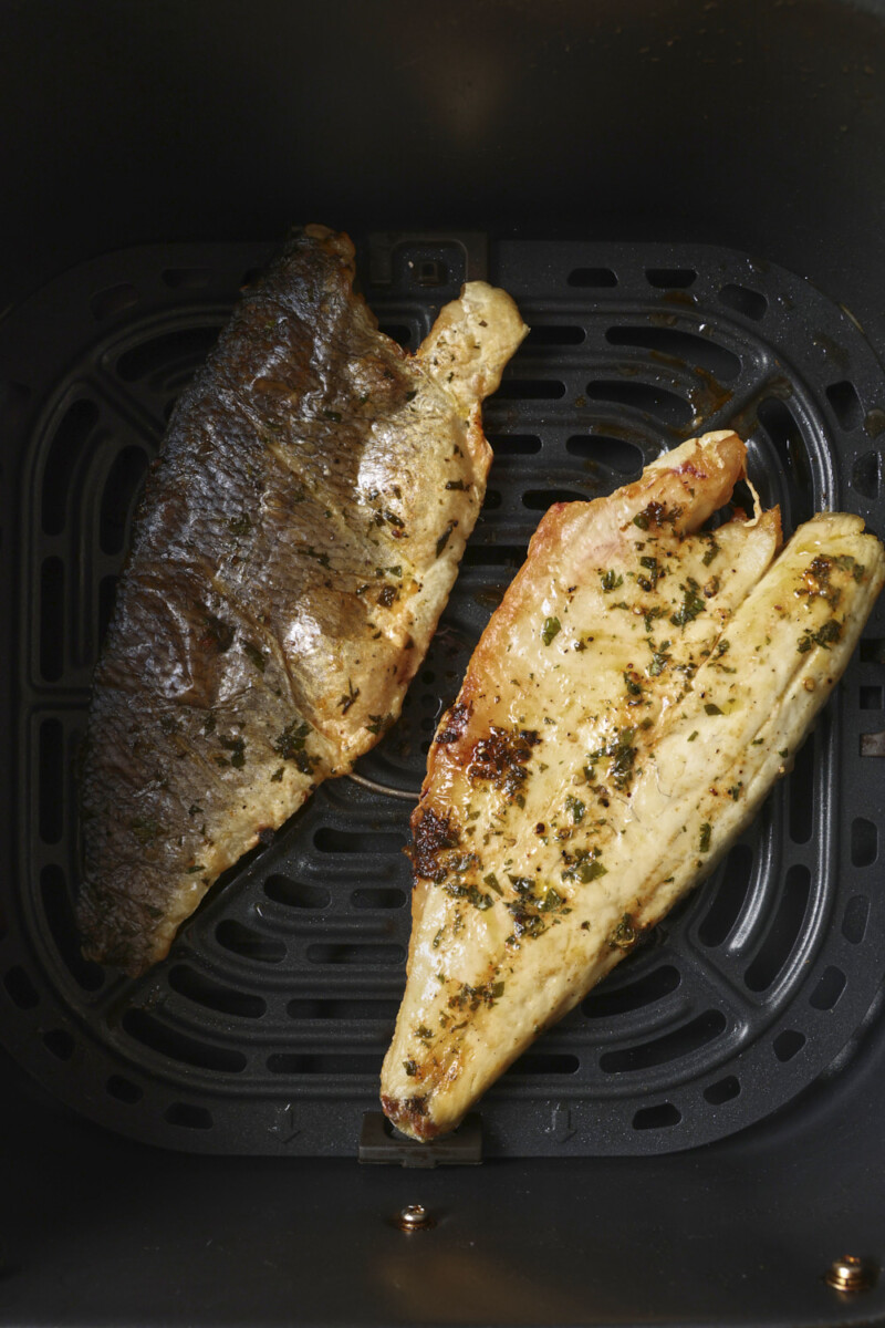 sea bass in an air fryer basket, one skin side up and one skin side down