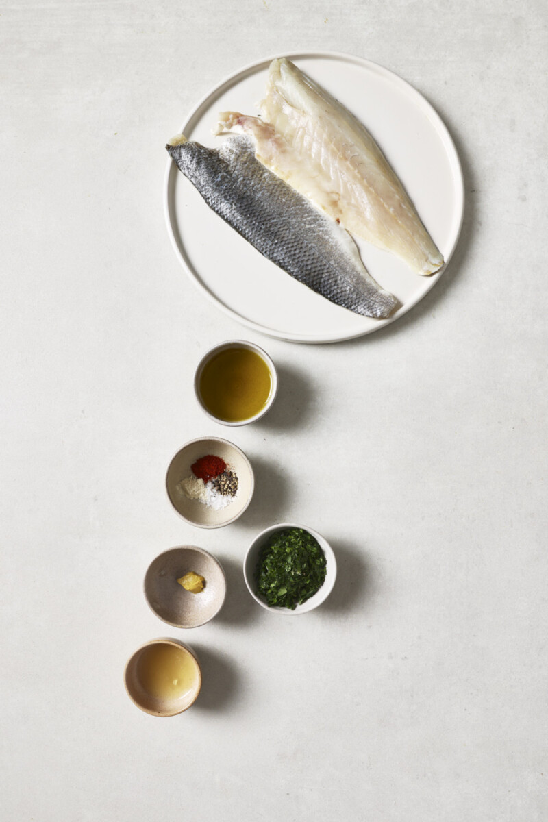 sea bass fillets on a plate, paprika, olive oil, and fresh parsley in small bowls
