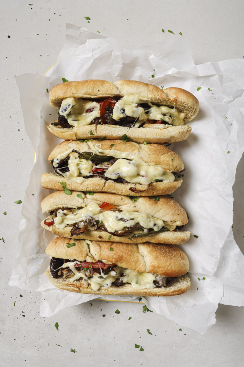 4 philly cheesesteaks arranged on parchment paper.