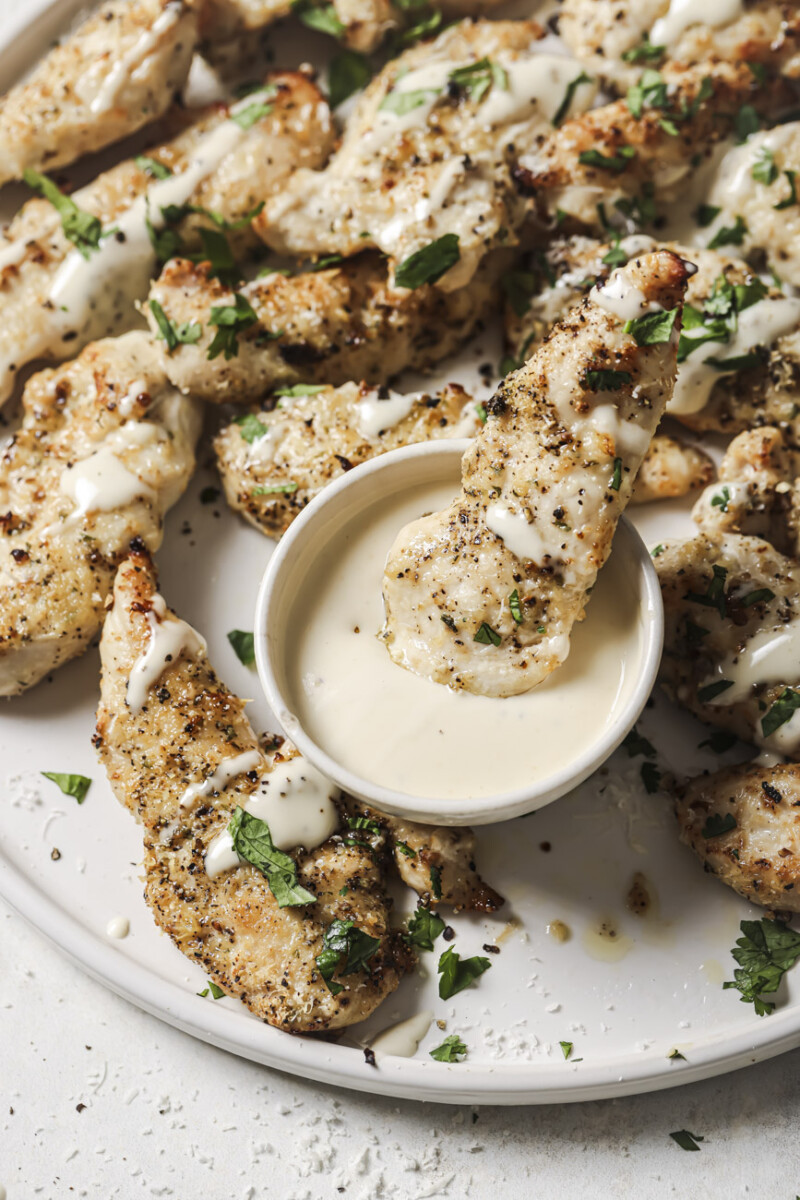 air fryer ranch chicken on a white plate and one piece dipped in ranch dressing