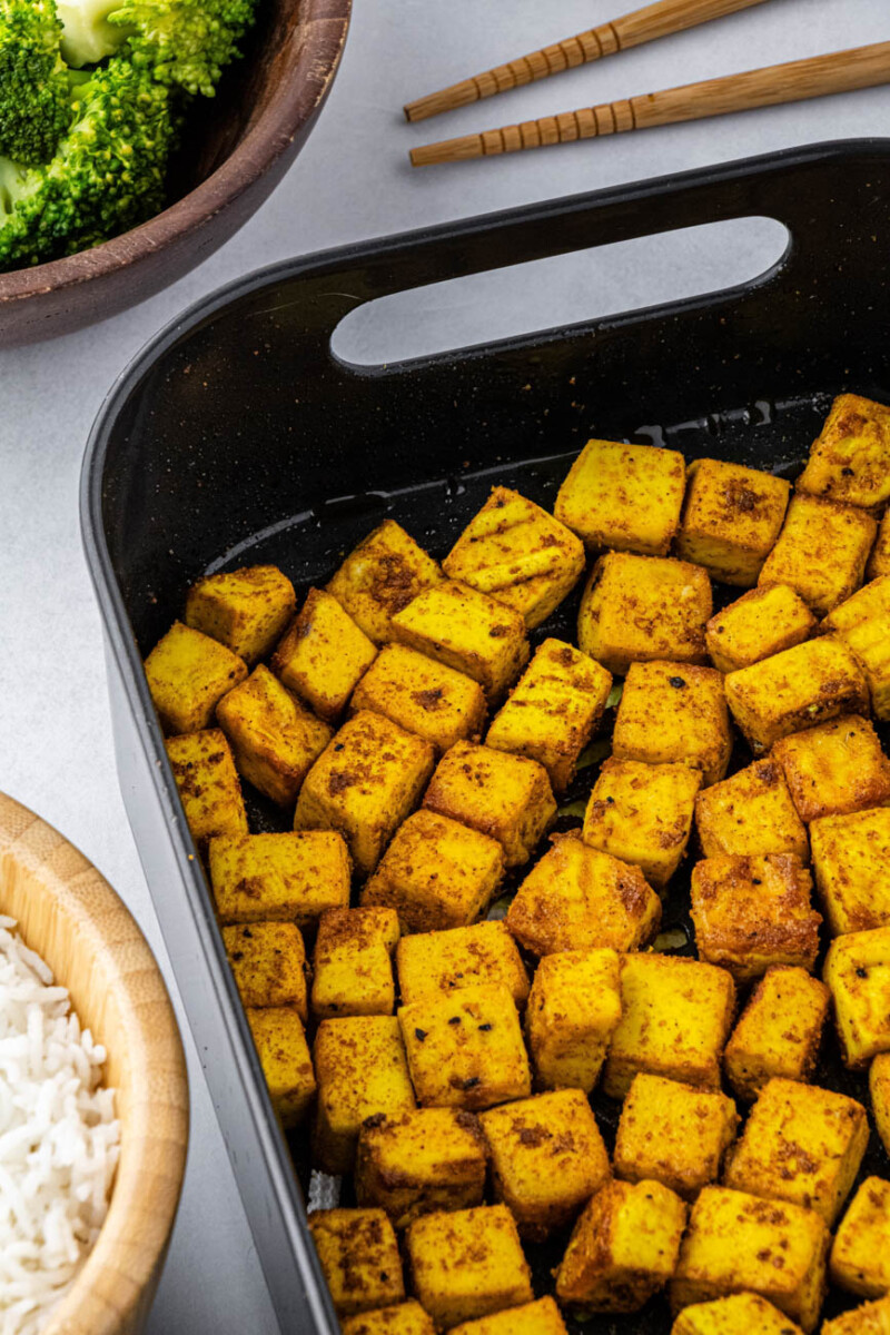 turmeric tofu in an air fryer basket with chopsticks and broccoli on the side