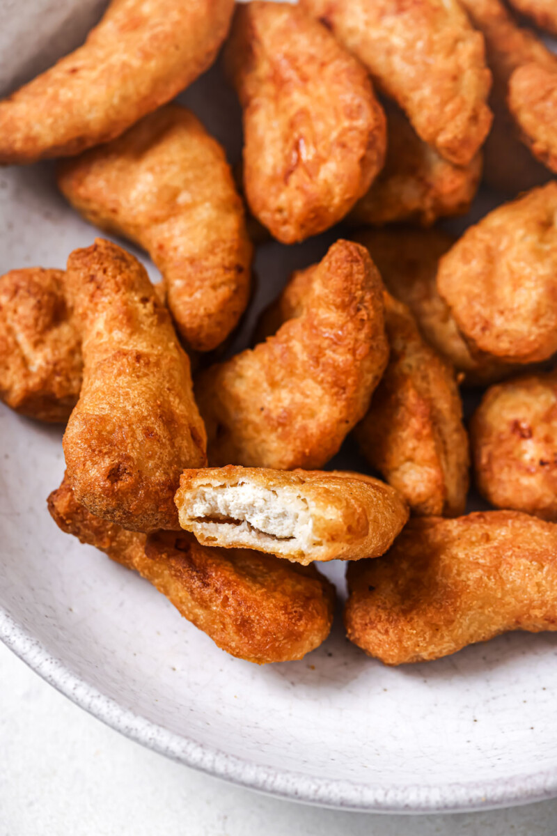 a white bowl full of cooked air fryer frozen chicken tenders, one with a bite taken