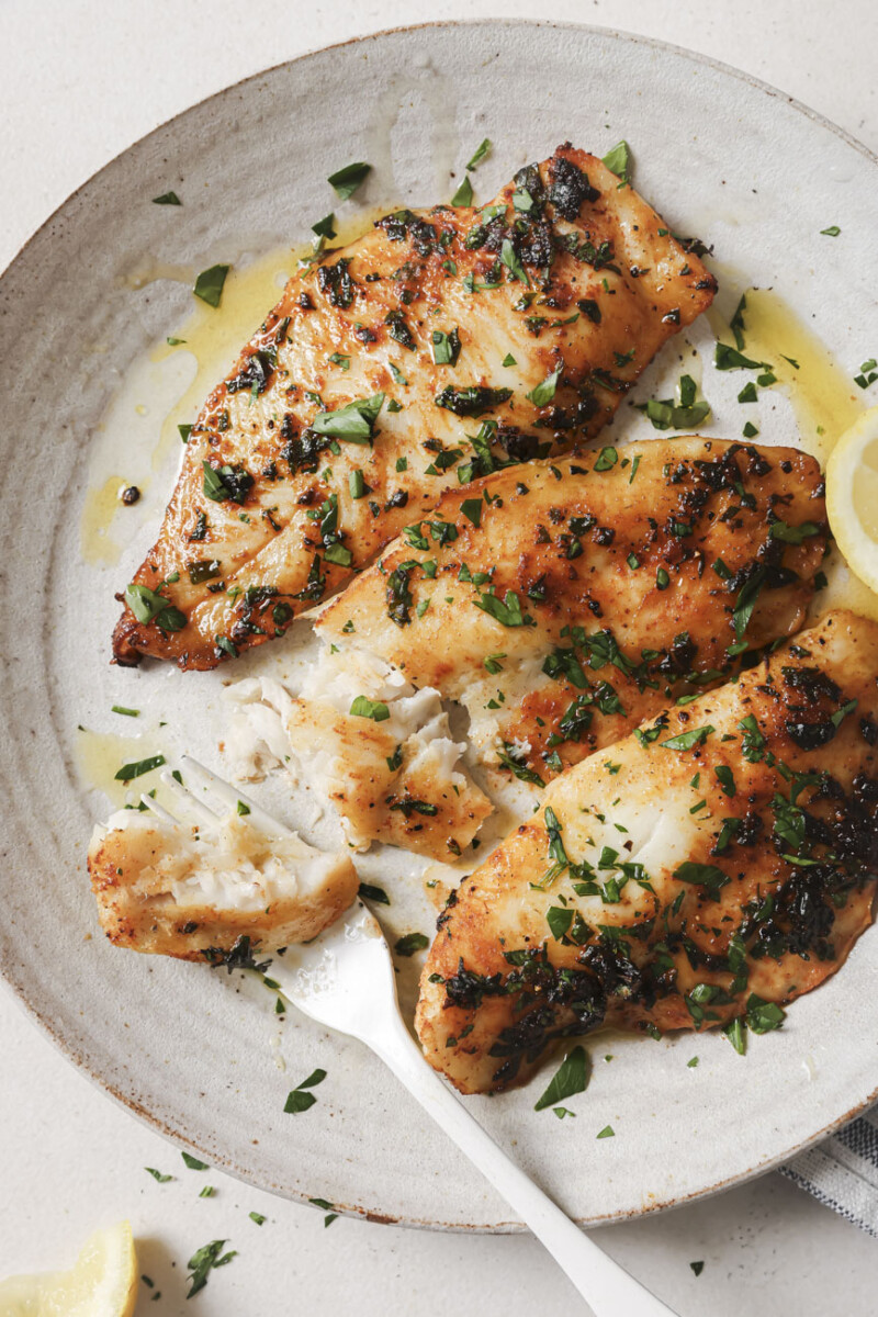 3 fillets of air fryer tilapia on a white plate with a white fork