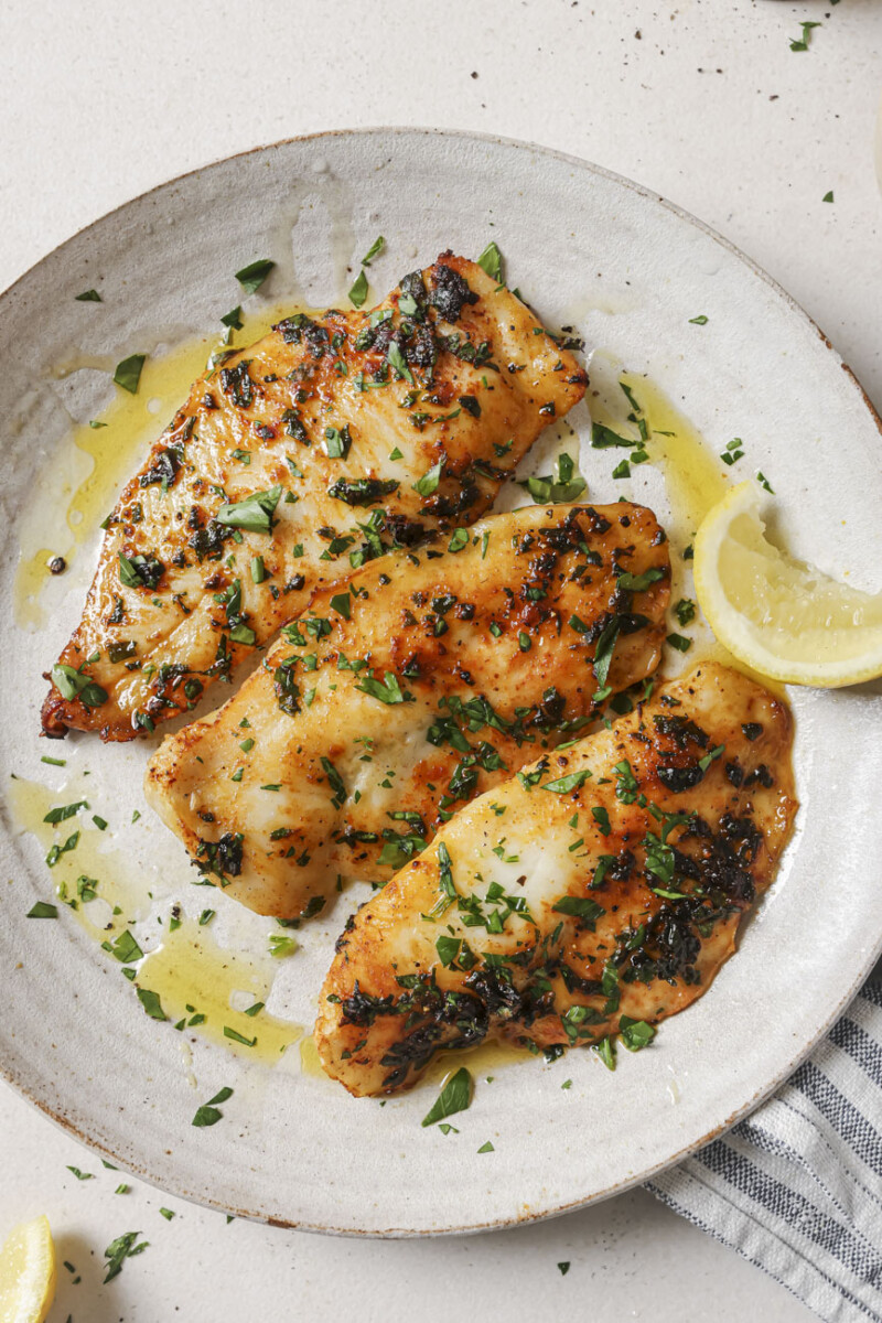 3 fillets of tilapia on a white plate with a lemon wedge