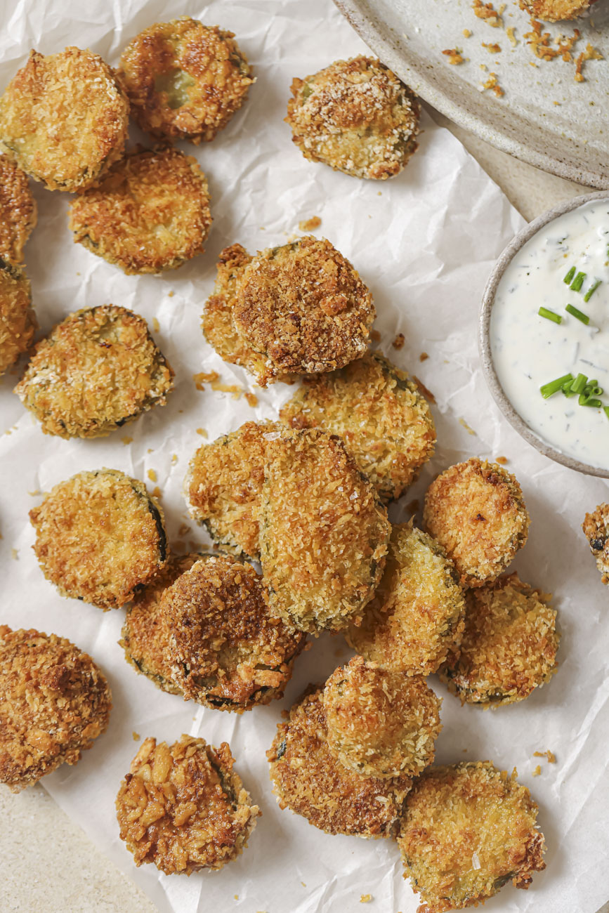 Air fried pickles on a piece of parchment with a small bowl of ranch dressing.