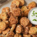 Close up view of a plate of air fried pickles with ranch.