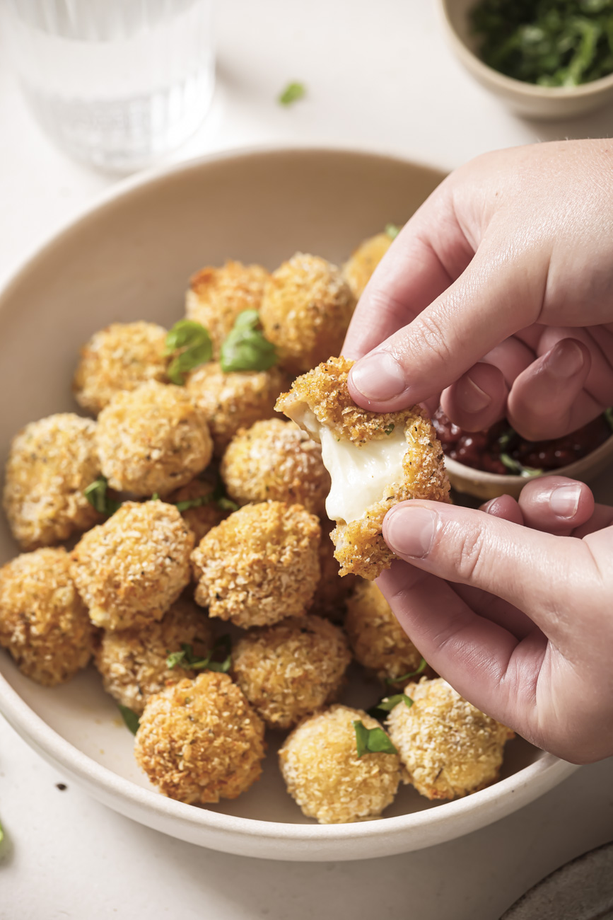 A pair of hands breaking open an air fried mozzarella ball.