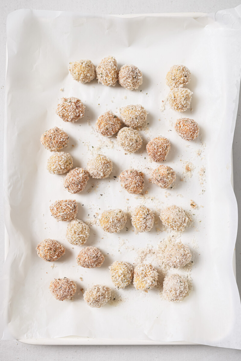 Breaded mozzarella balls on a parchment lined baking sheet.