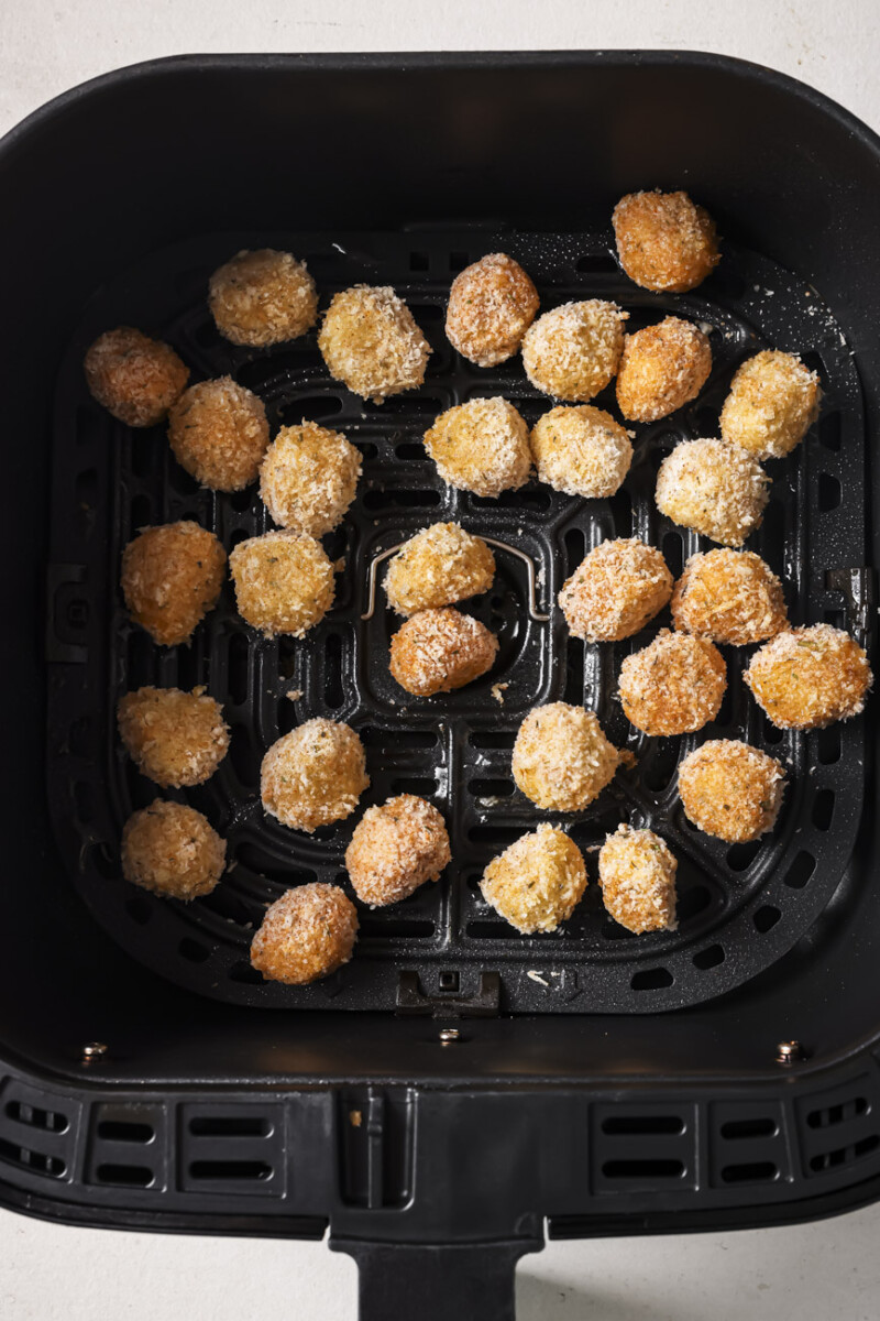 Breaded mozzarella balls in the air fryer basket.