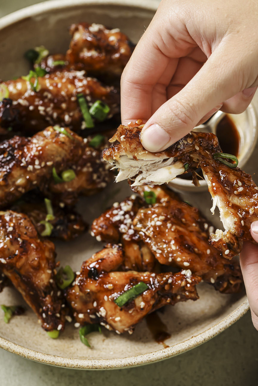 A pair of hands tearing apart a tender air fryer asian chicken wing.