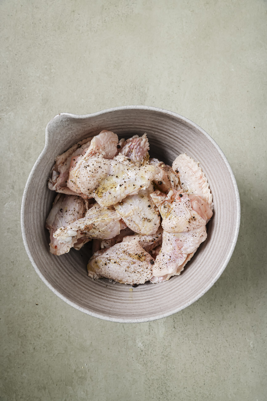 A bowl of raw chicken wings and seasonings.