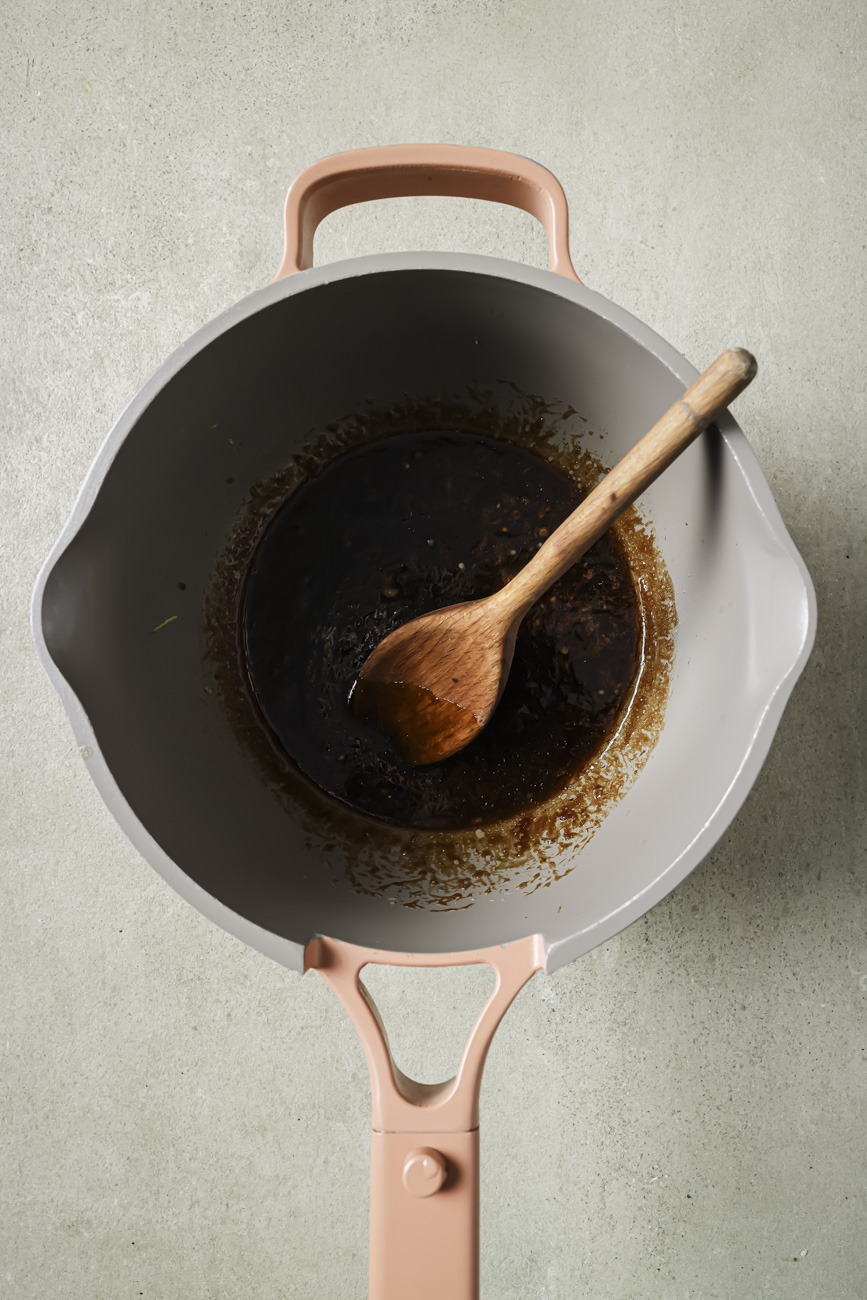 Cooking asian wing sauce in a pot with a wooden spoon.