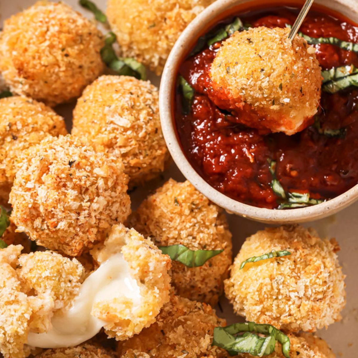 air fried mozzarella balls around a cup of marinara sauce, one of them dipped in the sauce.