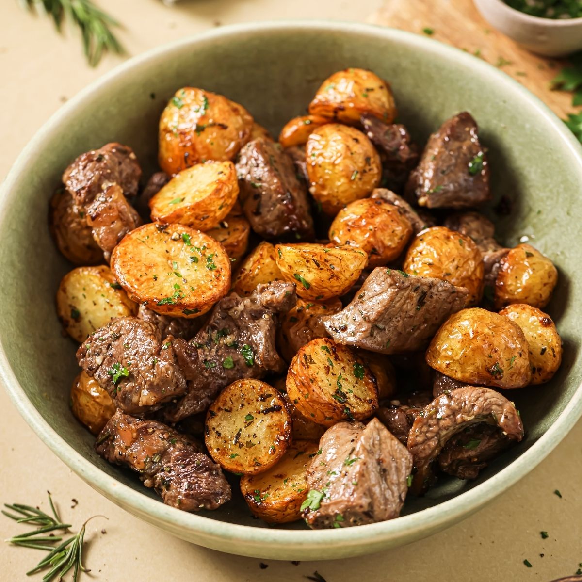 A green ceramic bowl full of air fryer steak bites and potatoes.