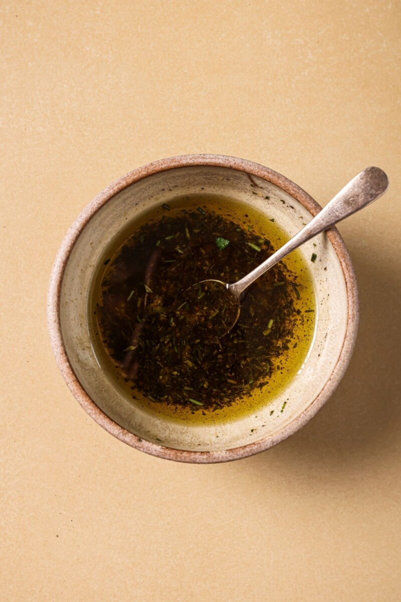 Mixing olive oil with herbs in a small ceramic bowl.