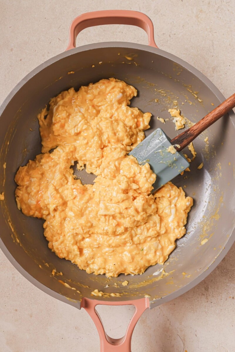 Scrambling eggs in a skillet with a blue spatula.