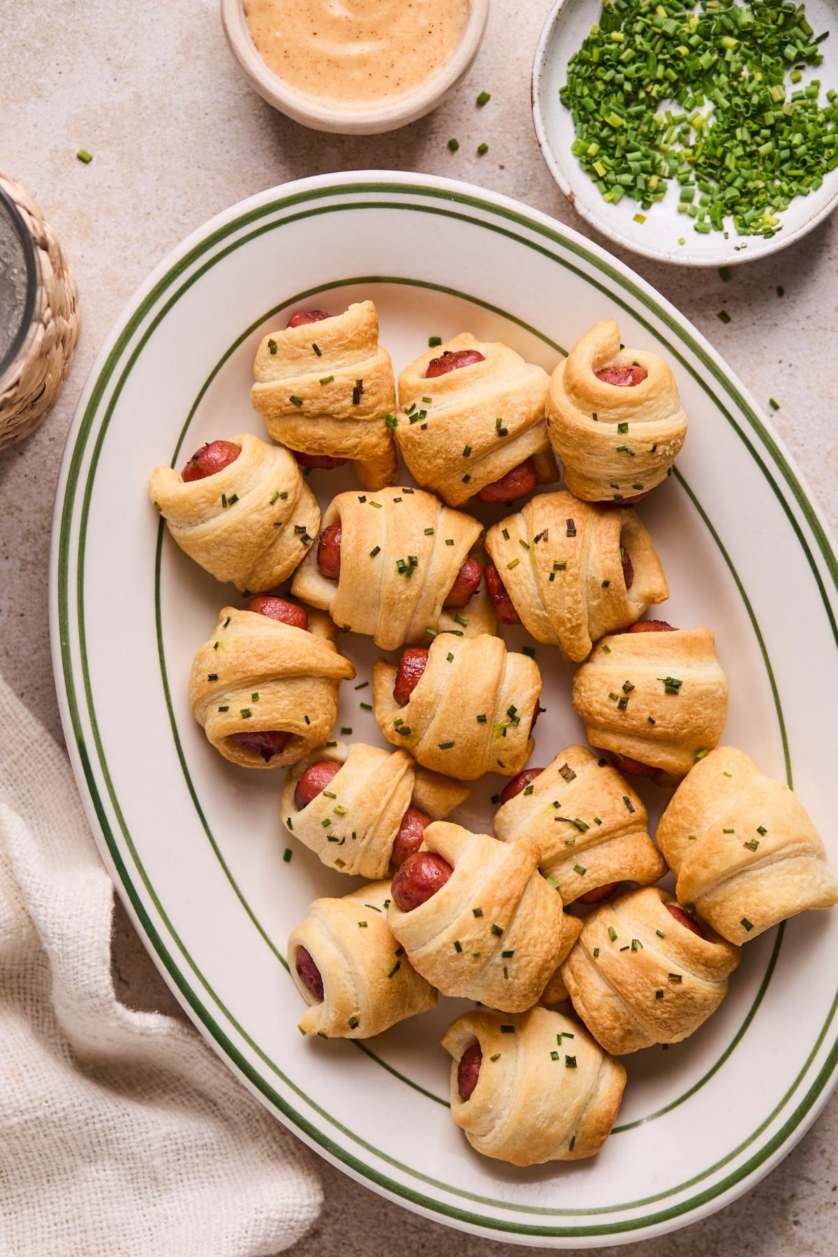 Pigs in a blanket on a platter with a dish of queso on the side.