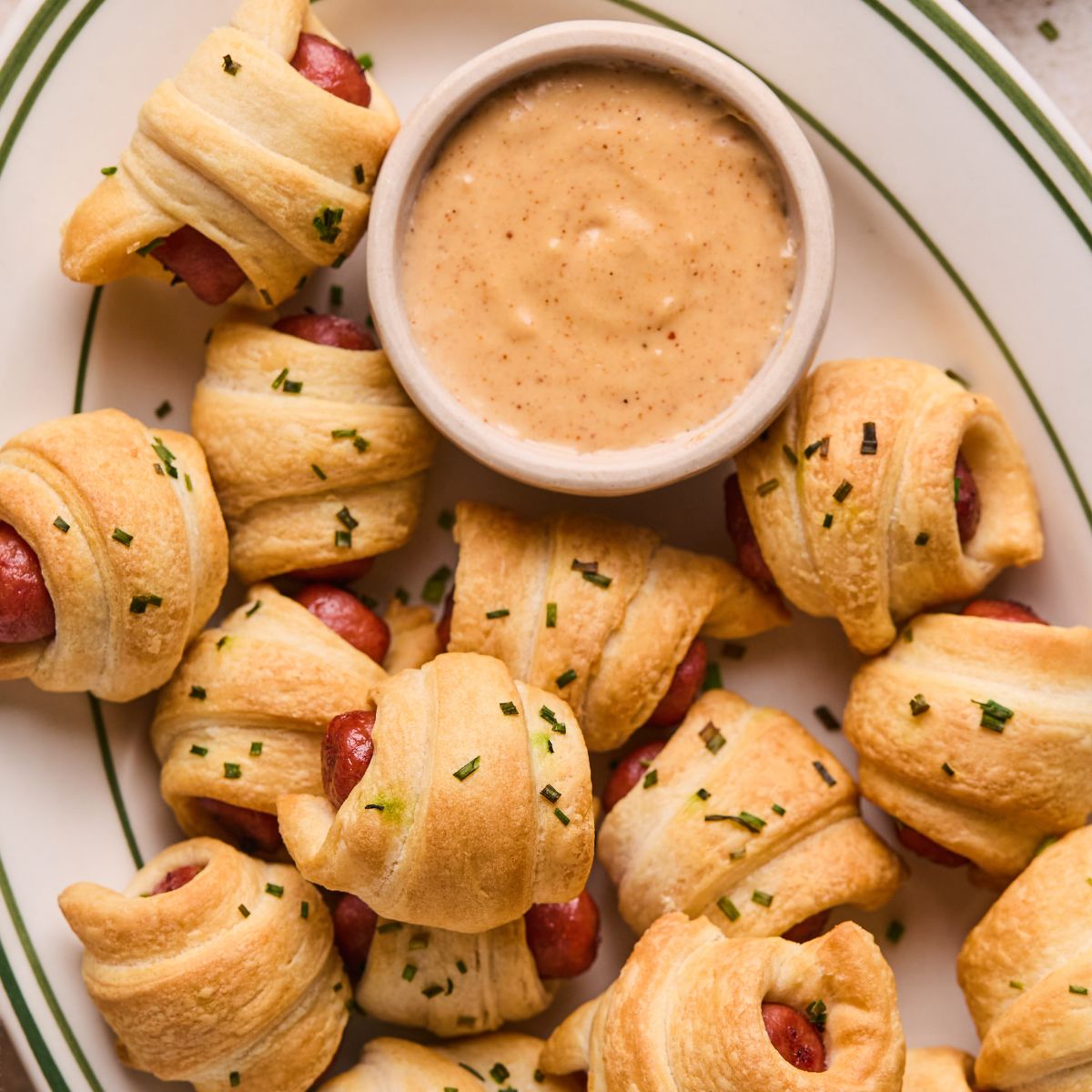 Pigs in a blanket on a serving platter with a dish of homemade queso sauce.