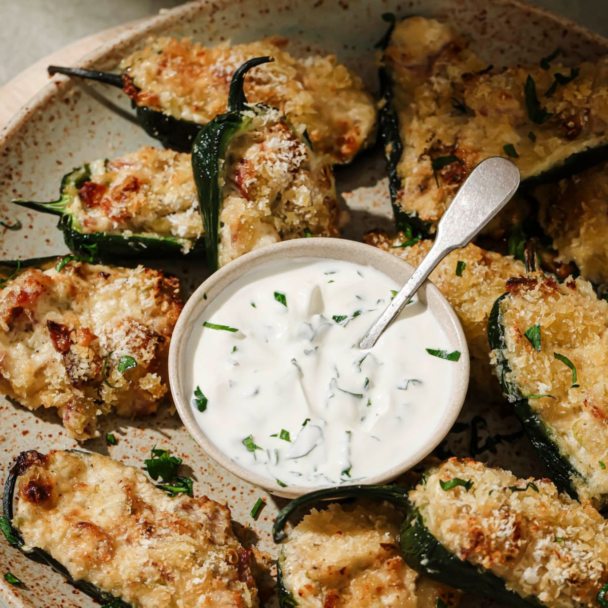 A close up shot of jalapeno poppers arranged around a small bowl of sour cream sauce.